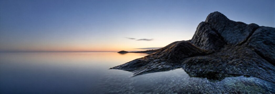 Serene rocky coastline beside calm sea at sunset with misty mountain ridge and spacious sky. Atmospheric nature banner with copy space for travel, wellness, and tourism design.