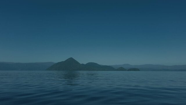 Low-angle view of the water surface with blue sky and Lake Toya's Nakajima Island in the distance