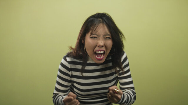 Woman with mouth open shouting, hands clutching head and fists raised in studio; raw frustration release.