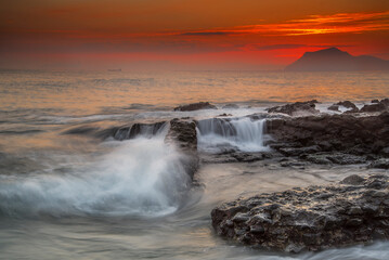 Fototapeta premium Sunbeams breaking through dark storm clouds over the sea with distant ships and rocky shore at sunset in Miono Cantabria