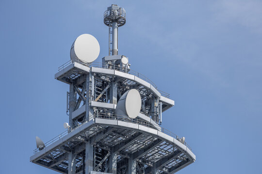 Multi-level matte gray telecommunications tower with lattice framework supporting radome covered parabolic dishes and vertical antennas set against a clear blue sky.