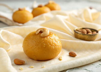 Fototapeta premium golden Besan Ladoo topped with a single cashew, sitting on a textured cream background.