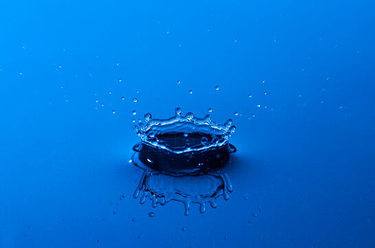 Close up f crown shaped water drop splash and reflection in blue light.