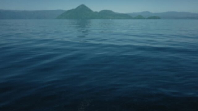 Low-angle view of the water surface with blue sky and Lake Toya's Nakajima Island in the distance