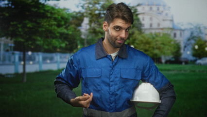 Fototapeta premium Man construction worker holding hardhat under arm and points finger to chest at building; confidence duty.