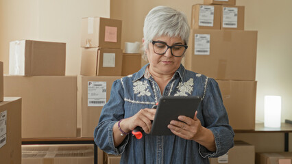 Woman scans cardboard packages with a handheld barcode scanner while holding and tapping a tablet in a packing building  focused productivity. © Krakenimages.com