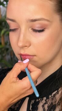 Professional makeup artist applies lip color with a cosmetic brush to a teenage girl, beauty styling, precise salon makeup application.