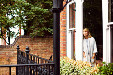 Fototapeta premium Morning, thinking and woman by door of holiday home for break, relax or vision and wellness. Daydream, idea and reflection of mature person on terrace of apartment for memories, nostalgia or planning
