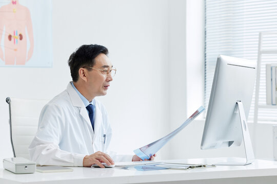 Male doctor reviewing paperwork at computer in medical office