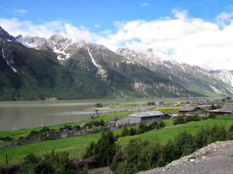 Scenic mountain lake with lush green fields and snow-capped peaks in the background