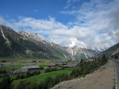 Scenic mountain valley with green fields and snow-capped peaks under blue sky
