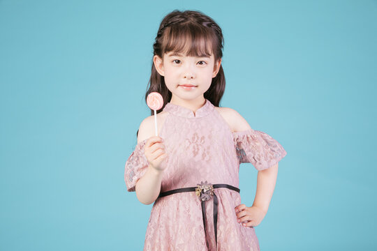 Little girl holding lollipop in pink dress against blue background