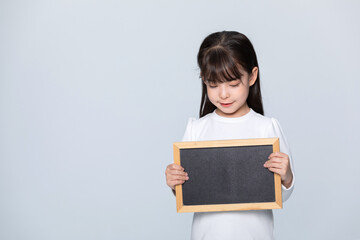 Little girl holding blank blackboard and looking down on gray background © LuuDieu