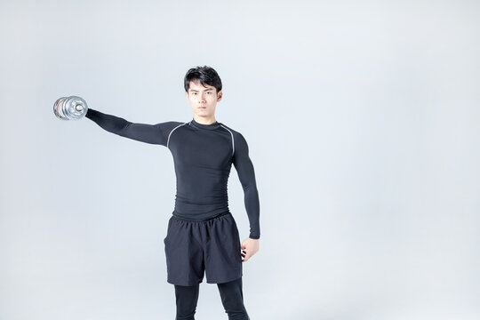 Athletic man performing dumbbell lateral raise in studio