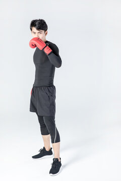 Athletic young man in boxing gloves posing in fighting stance in studio