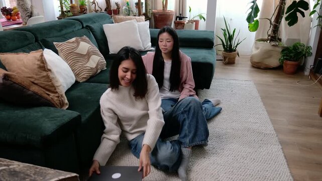 Young female friends watching entertainment on a computer while relaxing in the living room