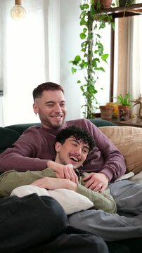 Affectionate male couple cuddling and laughing together while relaxing on the couch in the living room