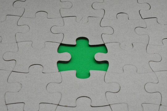 A cardboard jigsaw puzzle with one missing piece revealing a bright green surface underneath.
