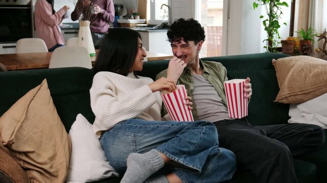Happy boyfriend and girlfriend relaxing on the couch, eating popcorn and watching television