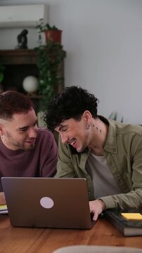 Two young male partners working from home on a laptop, one is on a business phone call