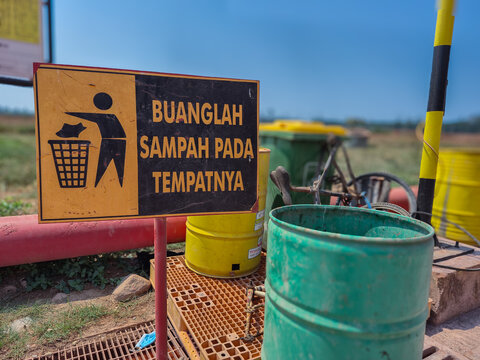A warning sign reading BUANGLAH SAMPAH PADA TEMPATNYA In English   DISPOSE OF TRASH PROPERLY  set against a background of trash bins in various colors corresponding to the type of waste.
