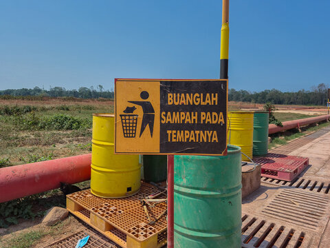 A warning sign reading BUANGLAH SAMPAH PADA TEMPATNYA In English   DISPOSE OF TRASH PROPERLY  set against a background of trash bins in various colors corresponding to the type of waste.
