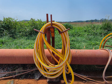 Yellow high pressure water hose coiled on stand at outdoor industrial and agricultural irrigation site with pipeline background