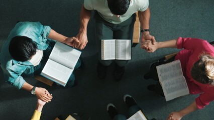Top down view of diverse people holding hand and sitting in circle with bible book on lap. Aerial...