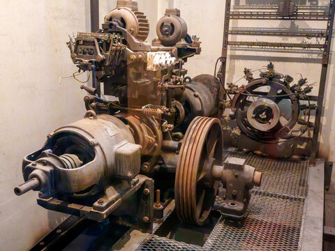 Vintage industrial electric motor with large pulley and mechanical components in an old engine room. Detailed historical engineering machinery and electrical wiring in a museum display.