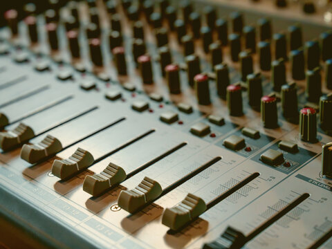 Close-up of a professional analog audio mixing console with faders and knobs in a recording studio. High angle view showing control sliders for sound engineering and music production.