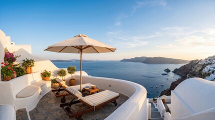 Fototapeta premium A cozy terrace with striped sun loungers, flowers, and an umbrella overlooks sailboats dotting the calm Aegean caldera at golden hour.