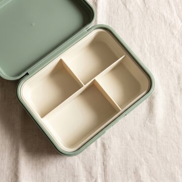 A top down view of a sage green plastic bento lunch box with four compartments