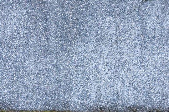 Dense blue gray pebble stones form a textured wall surface with tiny aggregate particles. Faint cracks and darker patches create subtle natural variations across the rough finish.