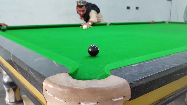 Billiard shot close up. Slow motion video of man hitting white cue ball on green cloth pool table. Black ball near corner pocket