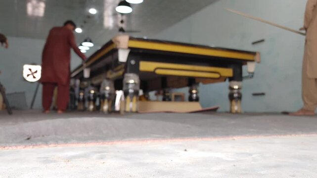 Snooker table in a club. Low angle shot of a yellow and black billiard table with players in the background. Slow motion b-roll footage