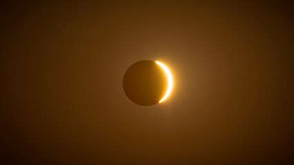 Thin solar crescent emerging through golden haze during solar eclipse, Spain. © PABLO
