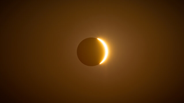 Thin solar crescent emerging through golden haze during solar eclipse, Spain.