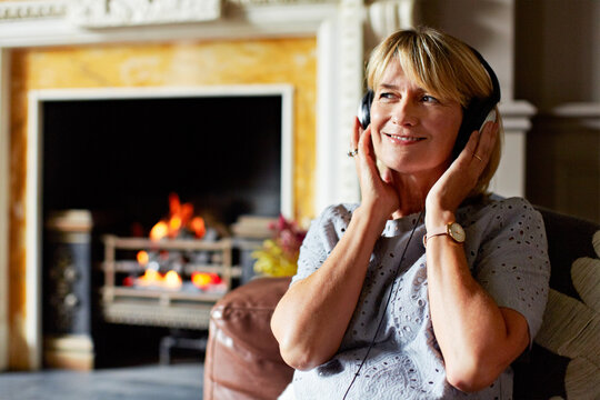 Smile, music and woman with headphones in home, streaming podcast or think of song by fireplace. Relax, happy and mature person with audiobook on couch, playlist idea or listening to radio on break