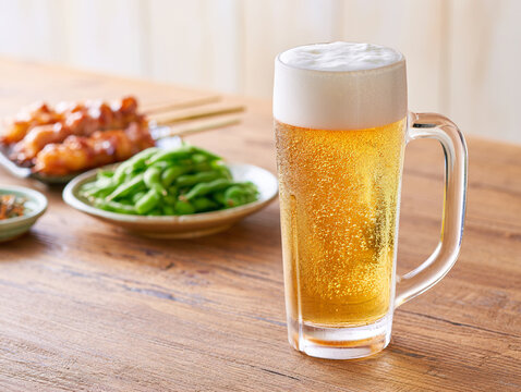 木製テーブルに置かれた冷たいビールと焼き鳥と枝豆