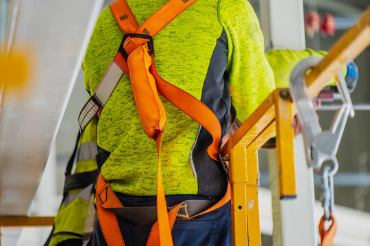 Construction worker wearing a certified safety harness and fall protection lanyard secured on an aerial work platform basket