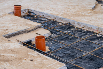 Naklejka premium Subgrade foundation construction showing a steel rebar grid, waterproof vapor barrier sheeting, and orange PVC utility pipes for plumbing