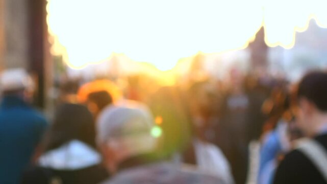 Anonymous crowd of people walking on a busy city street with a beautiful lens flare during a golden sunset. The shot is intentionally out of focus, creating an artistic, dreamlike effect