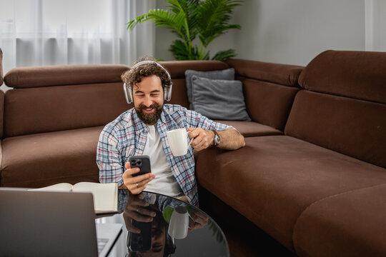 Man relaxing on sofa with headphones, coffee and phone while working from home
