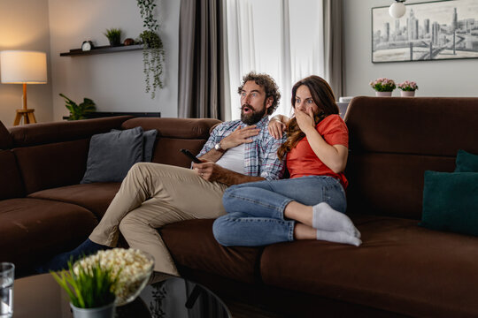Couple on sofa surprised while watching TV in cozy modern living room