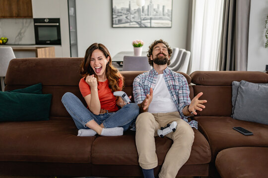 Couple playing video games on couch celebrating victory in cozy modern living room