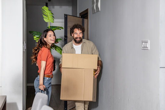 Young couple moving into new apartment carrying boxes and smiling in hallway
