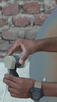 Close-up of hands adjusting a satellite dish LNB against a brick wall background