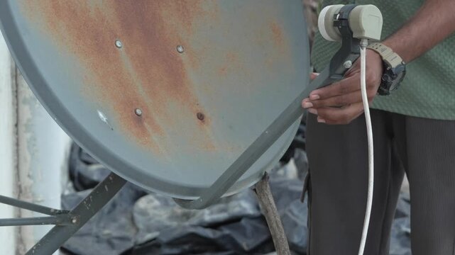 Person adjusting the LNB on a rusty DTH satellite dish antenna outdoors