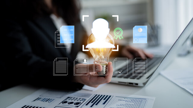 Business professional holding light bulb with digital icons overlay representing innovation, achievement, and technology in modern workspace Haptic.