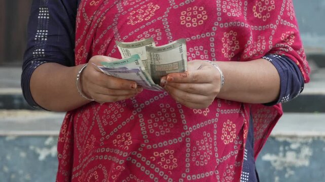 Woman in a red patterned ethnic outfit counting Indian Rupee currency notes
